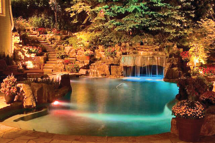 backyard pool and waterfall lit up at night