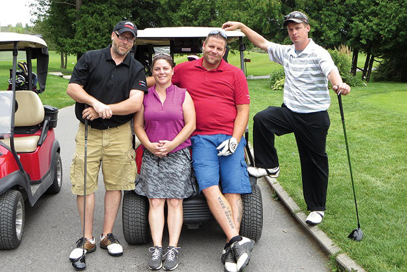 four golfers posing in front of a golf cart