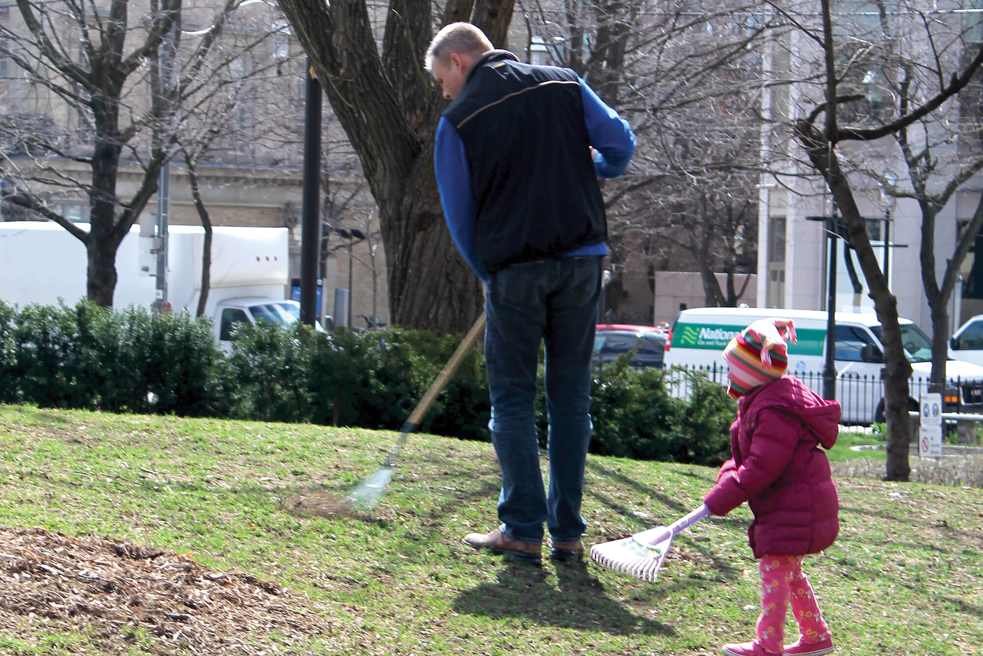 man and young child raking in a park