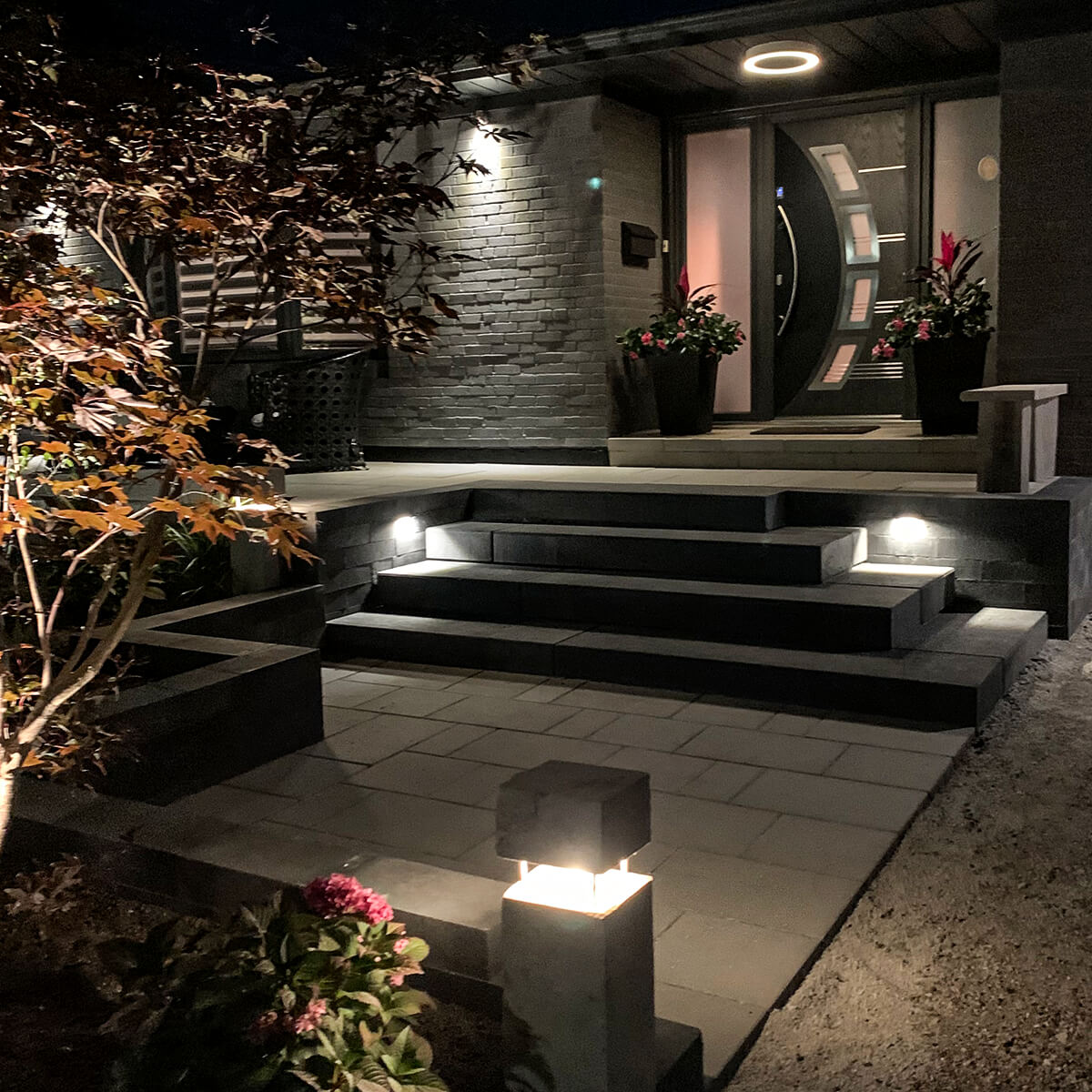 Front entrance of a modern-looking house at night with stone steps and landscape lighting