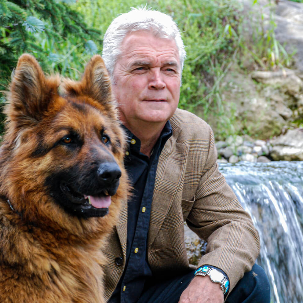man and dog pose beside a waterfall