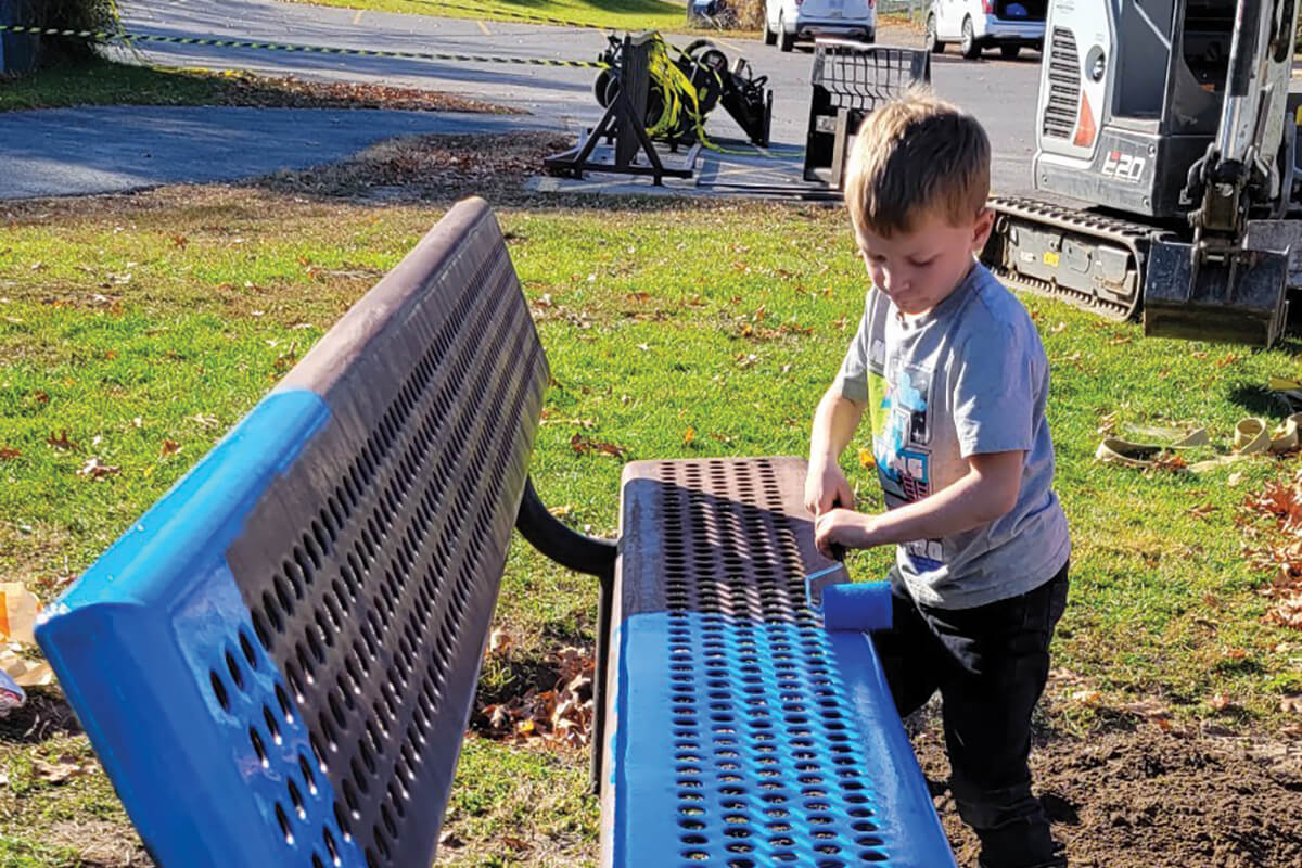 a young boy painting a bench blue